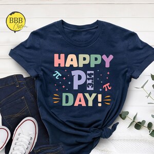 May include: A navy blue t-shirt with the text "HAPPY PI DAY!" in rainbow colors. The "PI" is stylized with the mathematical symbol and the number 3.14.