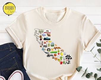 May include: Cream-colored t-shirt featuring a graphic of the California state outline filled with iconic imagery like a bear, mountains, and a Route 66 sign. The word "California" is written in script. The shirt is paired with blue jeans and white sneakers.