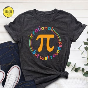 May include: A dark gray t-shirt with a colorful graphic of the mathematical symbol pi. The graphic is surrounded by a rainbow circle with the text "irrational but well rounded".