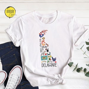 May include: White t-shirt with a graphic of the state of Delaware, featuring various icons representing the state. The text "The First State" and "DELAWARE" are included in the graphic.
