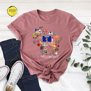 May include: A mauve t-shirt with a heart-shaped design featuring various icons representing Wisconsin. The icons include a cow, a cheese wedge, a beer stein, a fish, a football, and a red barn. The text "WISCONSIN" is written below the heart.