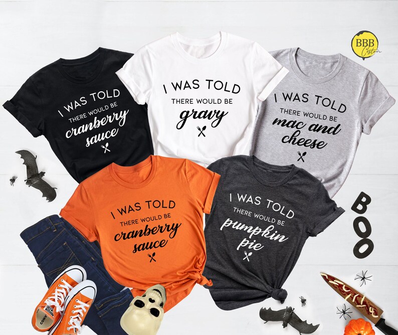 Op de afbeelding: Vijf verschillende T-shirts met een Thanksgiving-thema. Elk shirt heeft een ander voedsel erop, waaronder cranberry-saus, jus, macaroni en kaas, pompoentaart. De shirts zijn allemaal wit, zwart, grijs, oranje en donkergrijs.