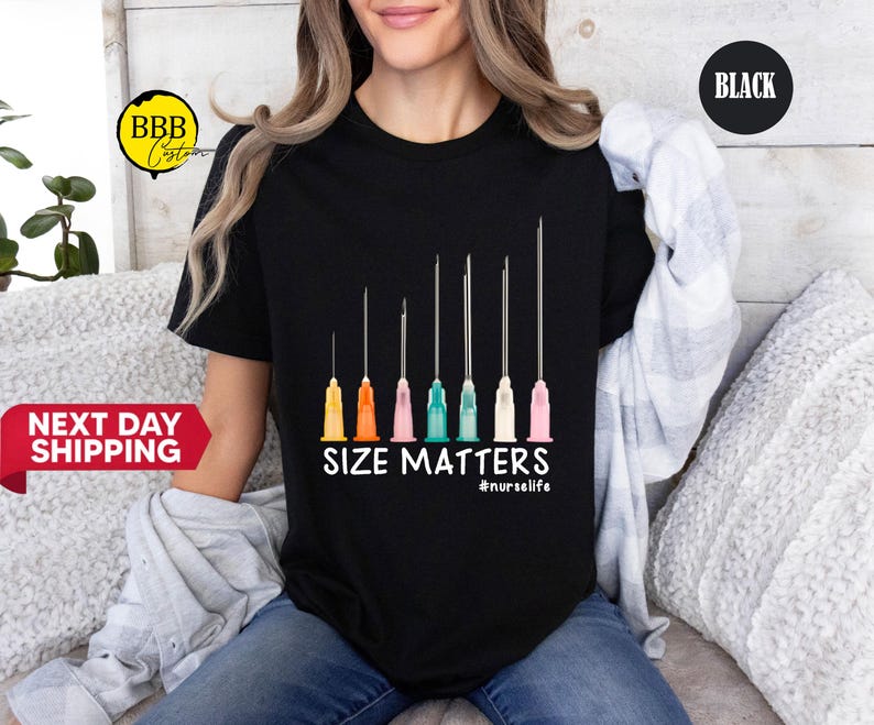 May include: Black t-shirt featuring a graphic of several syringes with colorful bases. The text "SIZE MATTERS" is printed below the syringes, with the hashtag "#nurselife" underneath. The shirt is a crew neck.