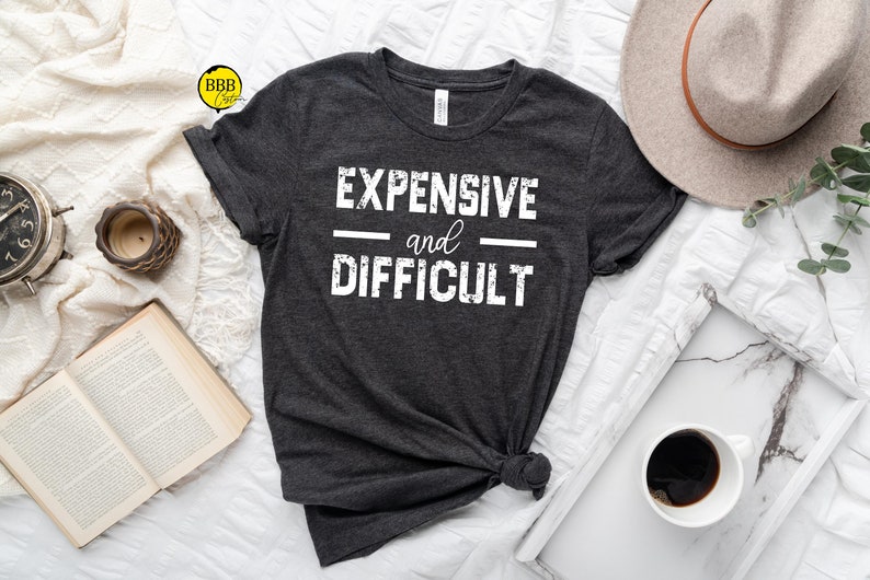 May include: A dark gray t-shirt with the text "EXPENSIVE and DIFFICULT" printed in white.