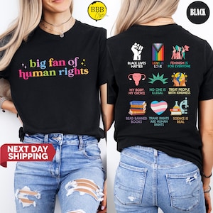 May include: Black t-shirt with the text "big fan of human rights" in colorful letters. The back of the shirt features various graphics and phrases, including "Black Lives Matter," "Love is Love," and "Feminism is for Everyone."