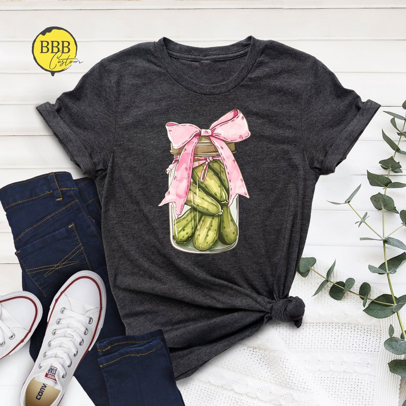 May include: A dark gray t-shirt with a graphic of a glass jar filled with green pickles and topped with a pink bow.
