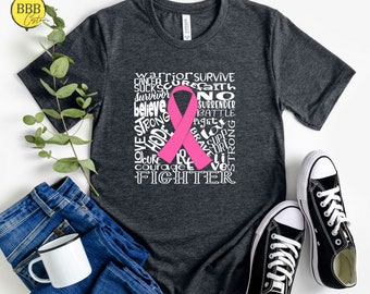 Könnte beinhalten: Ein dunkelgraues T-Shirt mit einem rosa Band und weißem Text, der "Warrior Survive, Sucks Cure Faith, Survivor, Believe, Strong, Cure, No Surrender, Battle, Fight, Love, Supp, Strong, Brave, Lite, Courage, Lives, Fighter" lautet.