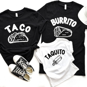 May include: Black t-shirts with white text and graphics. One shirt says "TACO" with a taco illustration, another says "BURRITO" with a burrito illustration, and a third says "TAQUITO" with a taquito illustration. A white baseball cap and black sneakers are also in the image.