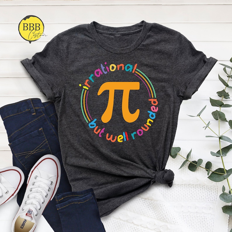 May include: A dark gray t-shirt with a colorful graphic of the mathematical symbol pi. The graphic is surrounded by a rainbow circle with the text "irrational but well rounded".