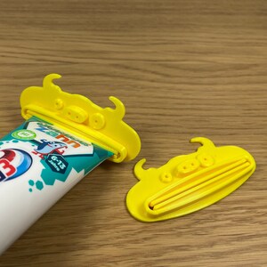 May include: A tube of Odol-med3 toothpaste with a yellow plastic toothpaste tube squeezer. The toothpaste tube is white with red and blue accents. The squeezer is shaped like a cartoon character.