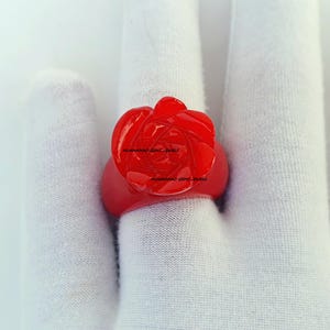 May include: A vibrant red ring featuring a carved rose design. The ring's band and the rose are a matching shade of red. The ring is shown on a white background.
