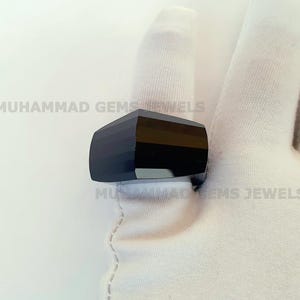 Könnte beinhalten: Ein schwarzer facettierter Edelsteinring. Der Ring liegt auf einem weißen Stoffhintergrund.