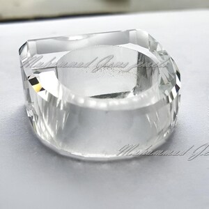 Könnte beinhalten: Ein klarer Glasringhalter mit quadratischer Basis und abgerundetem Oberteil. Der Halter ist aus Kristall und hat eine glatte, polierte Oberfläche.