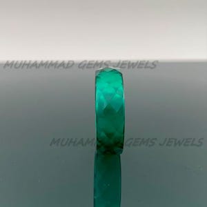 May include: A faceted, emerald-green gemstone ring. The ring is displayed vertically, showcasing its geometric cut and reflective surface. The text "MUHAMMAD GEMS JEWELS" is visible.