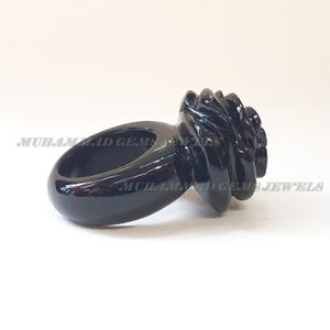 May include: A glossy black ring with a unique, textured design. The ring features a smooth band and a detailed, swirling centerpiece. The ring is set against a white background. The text "MUHAMMAD GEMS JEWELS" is visible.