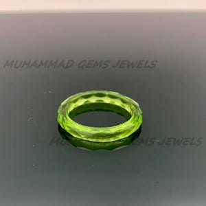 May include: A faceted, light green ring. The ring is a solid band with a geometric design. The text "MUHAMMAD GEMS JEWELS" is printed in white across the top of the image.