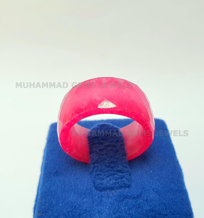May include: A faceted, bright pink ring with a small, silver-colored accent. The ring is displayed on a blue velvet surface. The ring is a bold statement piece.