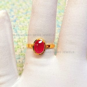 May include: A gold ring with a large, oval-shaped, red gemstone set in the center.