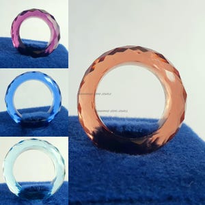 May include: A selection of faceted gemstone rings in shades of pink, blue, and peach. The rings are presented on a blue surface. The text "HAMMAD GEMS JEWELS" is visible on the peach ring.
