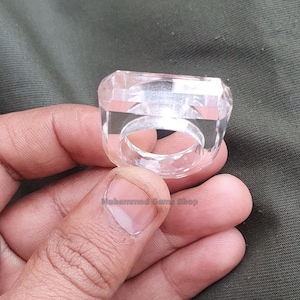 May include: A clear crystal ring with a square face. The ring is made of clear quartz and has a simple design.