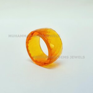 Puede incluir: Un anillo transparente de color naranja con un diseño facetado. El anillo está hecho de vidrio o plástico y tiene un acabado liso y pulido.