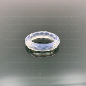 May include: A light-coloured, faceted ring with a geometric design. The ring has a translucent quality, reflecting light and creating a subtle shimmer. The ring is a piece of jewellery.