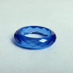 Peut inclure: Une bague bleu cobalt facettée. La bague présente un motif géométrique avec de multiples surfaces planes qui réfléchissent la lumière. La bague est une bande pleine, avec un intérieur lisse. La bague est d'une nuance de bleu vibrante.