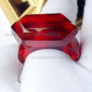 May include: A large, deep red, faceted gemstone ring. The ring is set in a simple, silver band. The gemstone is cut in a unique, geometric shape.