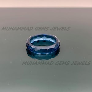 May include: A faceted, blue gemstone ring. The ring is a deep, transparent blue with a geometric design. The text "MUHAMMAD GEMS JEWELS" is printed on the surface.