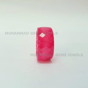 May include: A faceted, bright pink gemstone ring. The ring is a solid band with a geometric, multi-faceted design. The text "MUHAMMAD GEMS JEWELS" is printed on the image.
