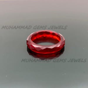 May include: A faceted, deep red ring. The ring has a geometric design with multiple flat surfaces. The ring is set against a dark background. The text "MUHAMMAD GEMS JEWELS" is visible.
