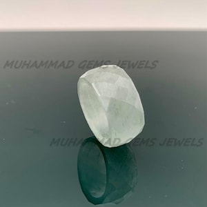 May include: A light green, faceted gemstone ring. The ring features a geometric design with multiple facets, reflecting light. The text "MUHAMMAD GEMS JEWELS" is visible in the background.