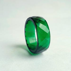 May include: A faceted, emerald-green ring. The ring has a geometric design with multiple facets that catch the light. The ring is a solid band of color, with a dark interior. The ring is a piece of jewelry.