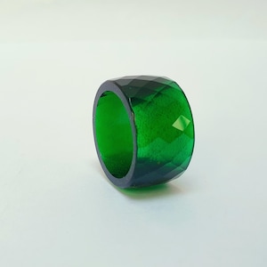 May include: A green faceted ring made of resin. The ring is a wide band with a geometric design.