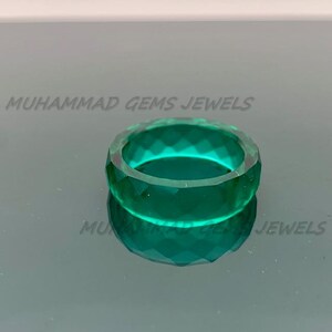 May include: A faceted, emerald-green ring. The ring is made of a translucent material and reflects light, creating a sparkling effect. The text "MUHAMMAD GEMS JEWELS" is visible.