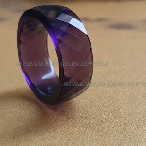 May include: A purple faceted ring made of glass. The ring is thick and has a wide band.