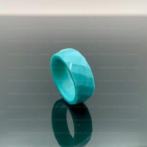 Op de afbeelding: Een turquoise ring met facetten. De ring heeft een geometrisch ontwerp met meerdere platte oppervlakken. De ring wordt getoond op een reflecterend oppervlak. Dit is een sieraad.