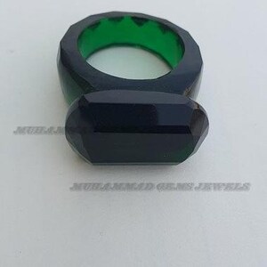 May include: A dark green ring with a large, faceted, black gemstone. The ring is made of a thick, green material.