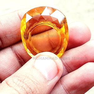 May include: A large, faceted, yellow gemstone ring. The ring is made of a single, large, yellow gemstone that is cut into a faceted shape. The ring is set in a simple, silver band.