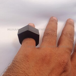 Könnte beinhalten: Ein schwarzer sechseckiger Ring, der an einem Finger getragen wird.