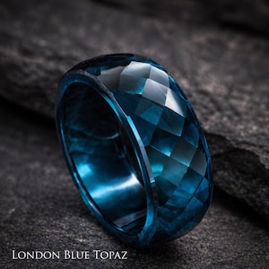 May include: A faceted London Blue Topaz ring. The ring is a deep teal blue color and has a geometric pattern. The ring is set against a dark gray, textured background. The text "LONDON BLUE TOPAZ" is at the bottom of the image.