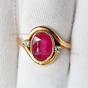 May include: A gold ring with a large oval ruby gemstone and two smaller diamond accents.