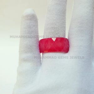 May include: A faceted, bright red ring is displayed on a white gloved hand. The ring has a geometric design and a flat top. The text "MUHAMMAD GEMS JEWELS" is visible on the glove.