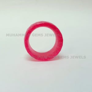 May include: A faceted, bright pink ring. The ring is a solid band with a geometric design. The text "MUHAMMAD GEMS JEWELS" is printed on the background.