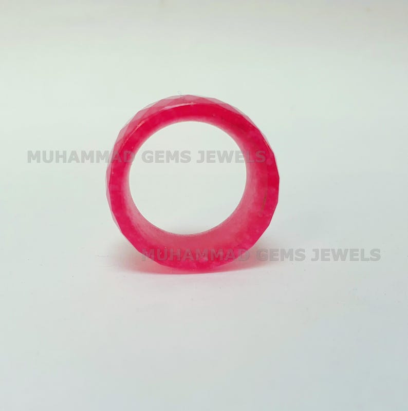May include: A faceted, bright pink ring. The ring is a solid band with a geometric design. The text "MUHAMMAD GEMS JEWELS" is printed on the background.