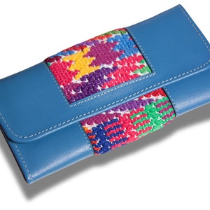 Puede incluir: Una cartera de cuero azul con una solapa bordada de colores. El bordado presenta un patrón geométrico en tonos de rosa, rojo, verde, amarillo y morado.