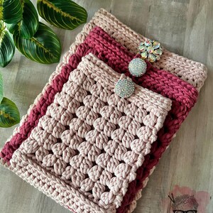 May include: A crocheted pink and burgundy clutch with a decorative crystal button. The clutch is made with a textured stitch and has a simple, elegant design.
