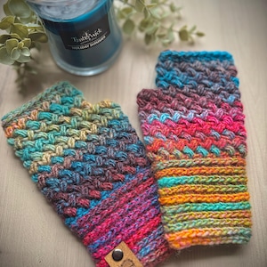May include: A pair of handmade, colorful fingerless gloves. The gloves are knitted with a variety of yarn colors, including blue, pink, and orange. A small leather tag with a button is attached to one of the gloves.