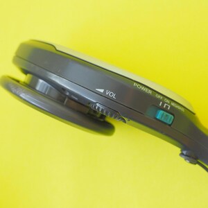 K&ouml;nnte beinhalten: Ein dunkelgraues tragbares Audioger&auml;t mit einem Lautst&auml;rkeregler, einem t&uuml;rkisfarbenen Netzschalter mit der Beschriftung POWER OFF ON und dem Schriftzug MEGABASS. Das Ger&auml;t hat eine abgerundete, ergonomische Form mit einem runden Lautsprecher.