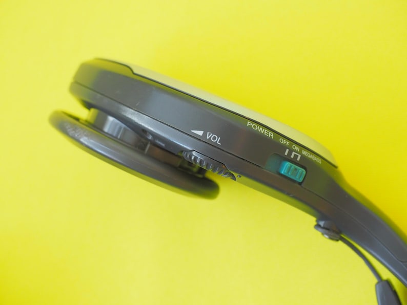 K&ouml;nnte beinhalten: Ein dunkelgraues tragbares Audioger&auml;t mit einem Lautst&auml;rkeregler, einem t&uuml;rkisfarbenen Netzschalter mit der Beschriftung POWER OFF ON und dem Schriftzug MEGABASS. Das Ger&auml;t hat eine abgerundete, ergonomische Form mit einem runden Lautsprecher.